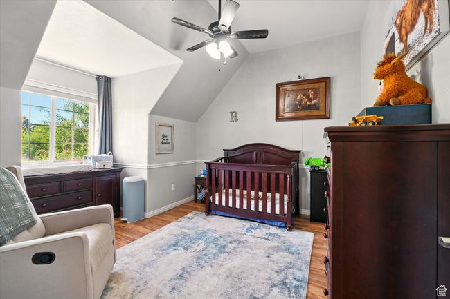 Bedroom featuring wood finished floors, a nursery area, lofted ceiling, a ceiling fan, and baseboards | Image 26