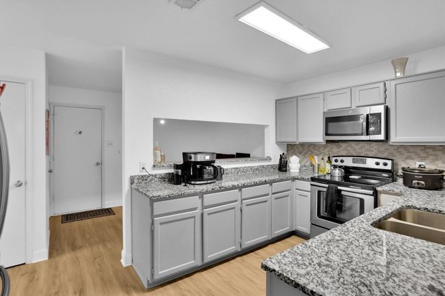 Kitchen featuring stainless steel appliances, gray cabinetry, light wood finished floors, light stone countertops, and decorative backsplash | Image 15