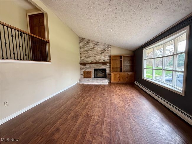 Unfurnished living room with vaulted ceiling, a textured ceiling, hardwood / wood-style flooring, and baseboard heating | Image 12