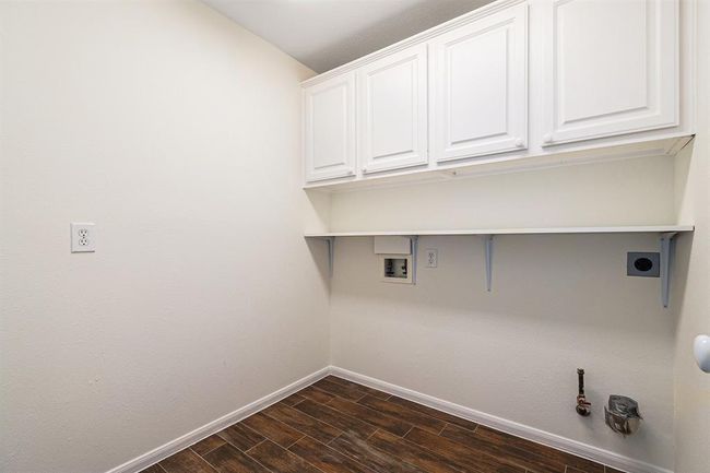 A large utility room has cabinets for storage, a shelf for pretty things and more of the easy to maintain wood look tile flooring! | Image 23