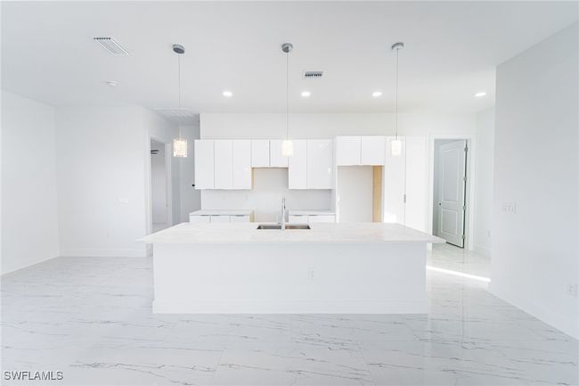 Kitchen featuring hanging light fixtures, white cabinetry, a kitchen island with sink, and sink | Image 4
