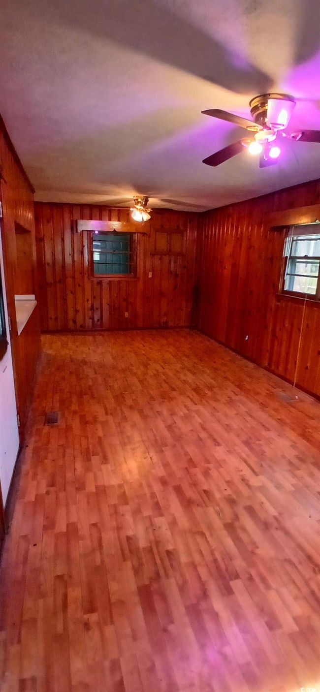 Unfurnished living room with wooden walls, wood finished floors, and a ceiling fan | Image 20