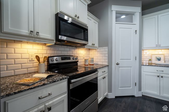 Kitchen featuring appliances with stainless steel finishes, backsplash, dark stone counters, white cabinetry, and dark wood-style floors | Image 5