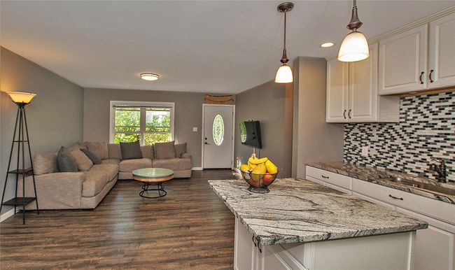 Kitchen featuring backsplash, light stone counters, dark wood-type flooring, sink, and decorative light fixtures | Image 7