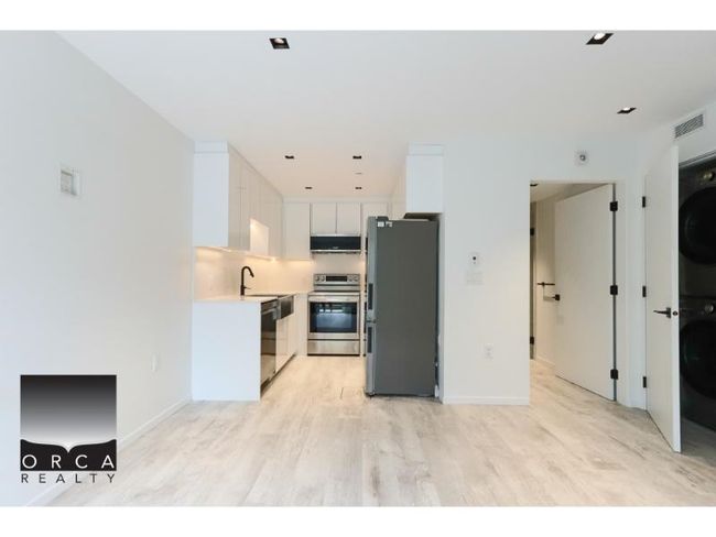 Kitchen featuring stainless steel appliances, stacked washer / drying machine, light wood finished floors, light countertops, and ventilation hood | Image 4