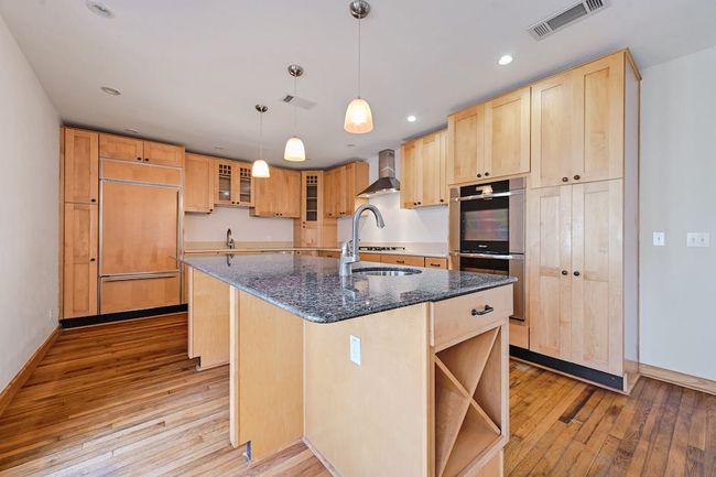 Kitchen with light brown cabinets, visible vents, stainless steel double oven, paneled refrigerator, and wall chimney exhaust hood | Image 6