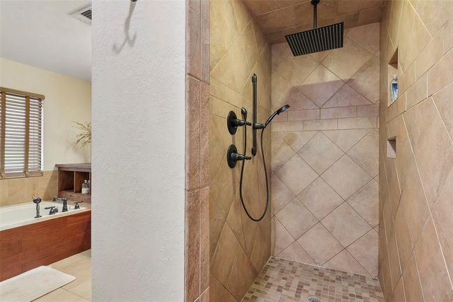 This bathroom features a spacious walk-in shower with elegant tiling and a modern rain showerhead, complemented by a cozy bathtub with wooden accents and a large window for natural light. | Image 29