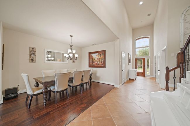 This photo showcases a bright, open foyer with a high ceiling and tile flooring, leading into a formal dining area with elegant wood flooring and a stylish chandelier. The space is well-lit and inviting. | Image 10