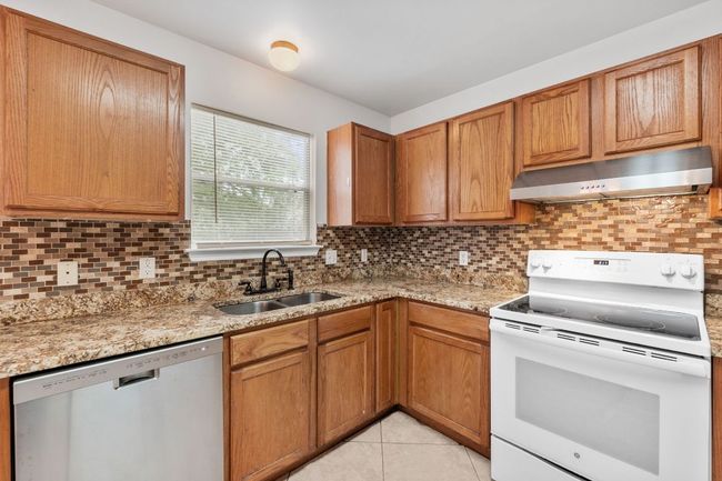 Kitchen with white range with electric stovetop, stainless steel dishwasher, extractor fan, a sink, and decorative backsplash | Image 15