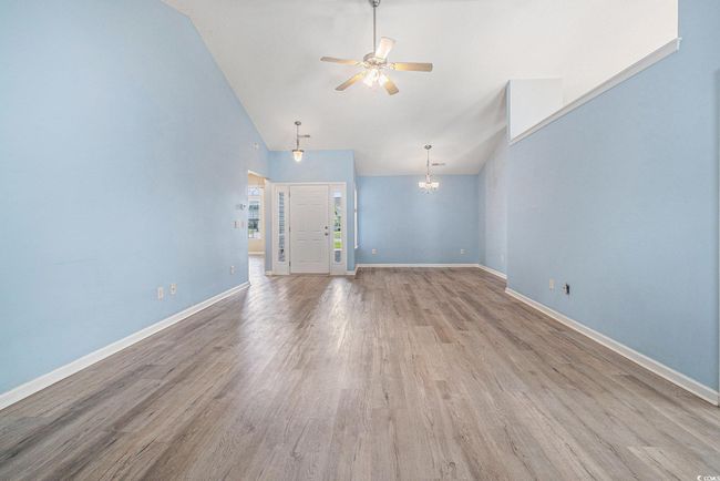Unfurnished living room with ceiling fan, wood finished floors, a chandelier, and high vaulted ceiling | Image 10