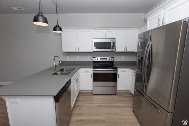 Kitchen featuring appliances with stainless steel finishes, a sink, a peninsula, light wood-style floors, and white cabinetry | Image 7