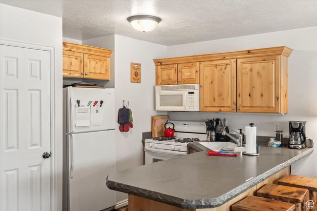 Kitchen featuring a breakfast bar, white appliances, a sink, a peninsula, and dark countertops | Image 4