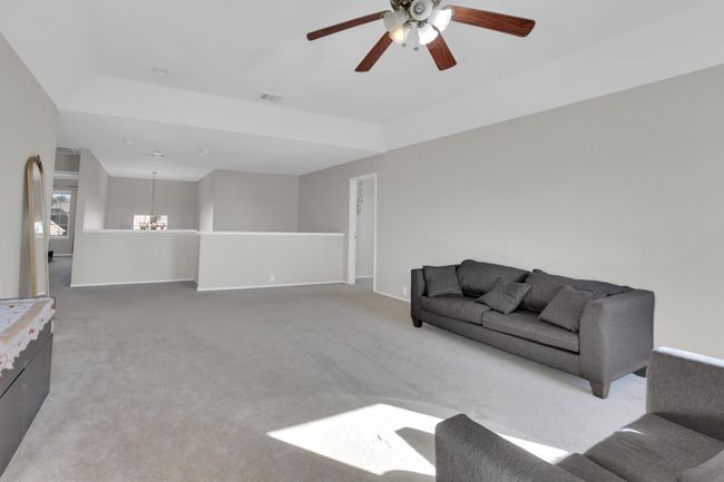 Living room with light carpet, ceiling fan with notable chandelier, visible vents, and baseboards | Image 26