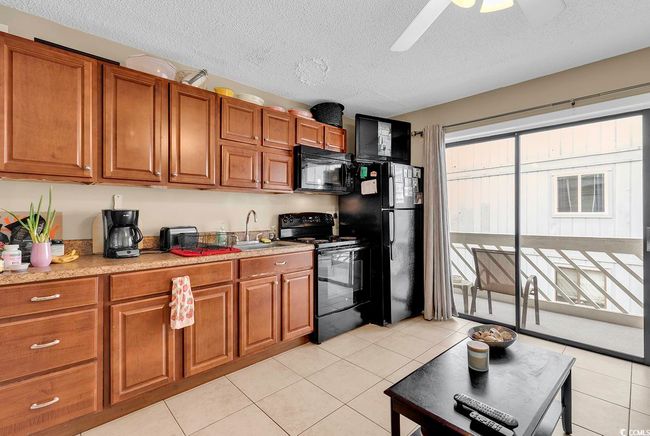 Kitchen with light tile patterned floors, a ceiling fan, brown cabinetry, a sink, and black appliances | Image 25