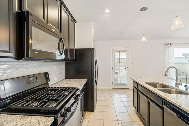 Kitchen with a sink, black microwave, dishwashing machine, gas range oven, and light tile patterned floors | Image 13