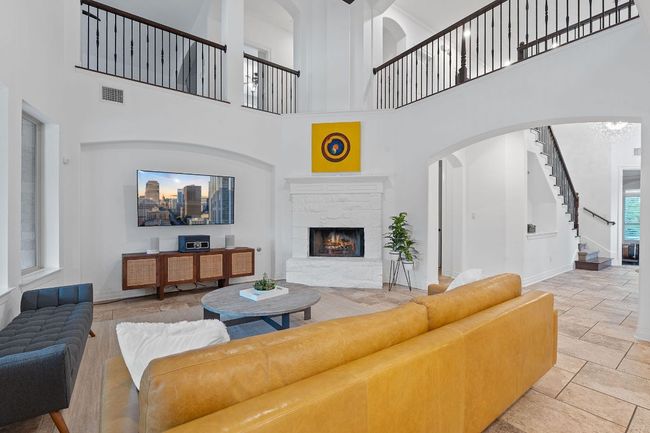 Living room with a towering ceiling, a stone fireplace, stairs, stone tile flooring, and arched walkways | Image 31