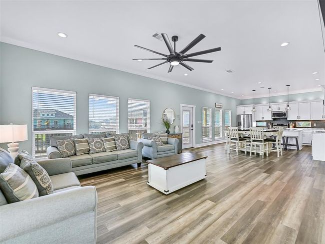 Step inside the full-panel glass door to a bright and airy open-concept living area with stylish coastal finishes, durable luxury vinyl plank floors, and plenty of seating—ideal for entertaining or hosting large groups comfortably. | Image 7