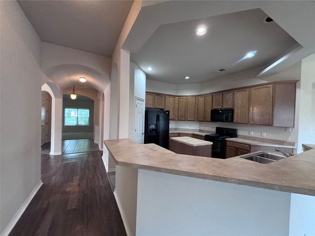 Kitchen featuring black appliances, arched walkways, light countertops, dark wood-type flooring, and a peninsula | Image 12