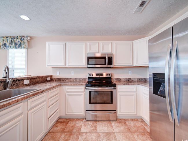Kitchen featuring stainless steel appliances, a textured ceiling, white cabinetry, and stone countertops | Image 20