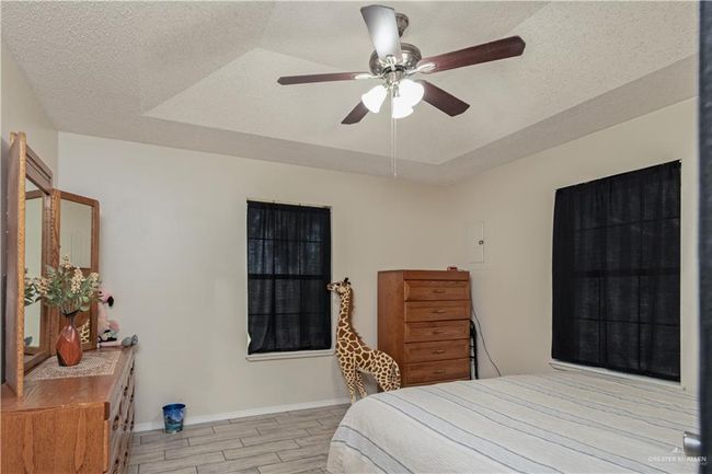 Bedroom with wood finish floors, baseboards, a raised ceiling, a textured ceiling, and ceiling fan | Image 12