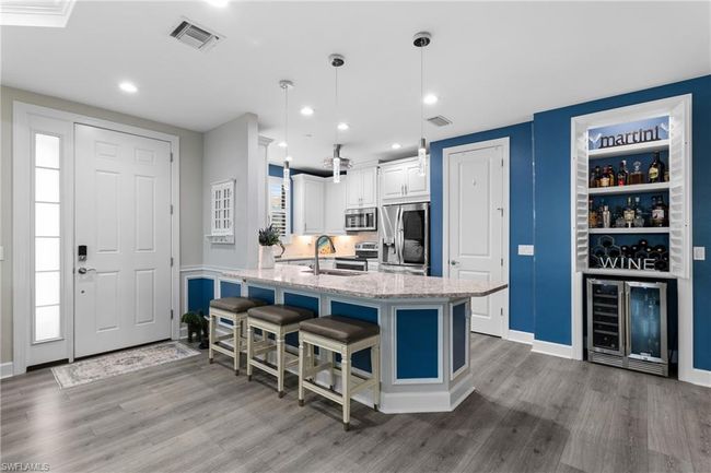 Kitchen with stainless steel appliances, beverage cooler, wood finished floors, light stone countertops, and a kitchen bar | Image 6