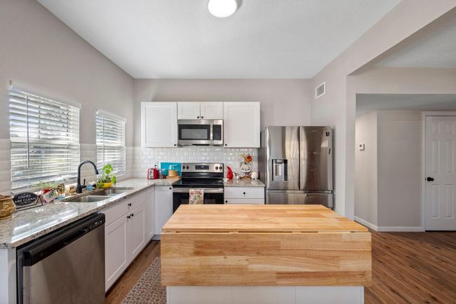 Kitchen featuring dark wood-style floors, a sink, butcher block counters, appliances with stainless steel finishes, and visible vents | Image 5