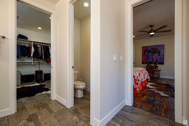 Primary En-Suite Bathroom with connected water closet, walk in closet, a ceiling fan, a textured ceiling, and baseboards | Image 22