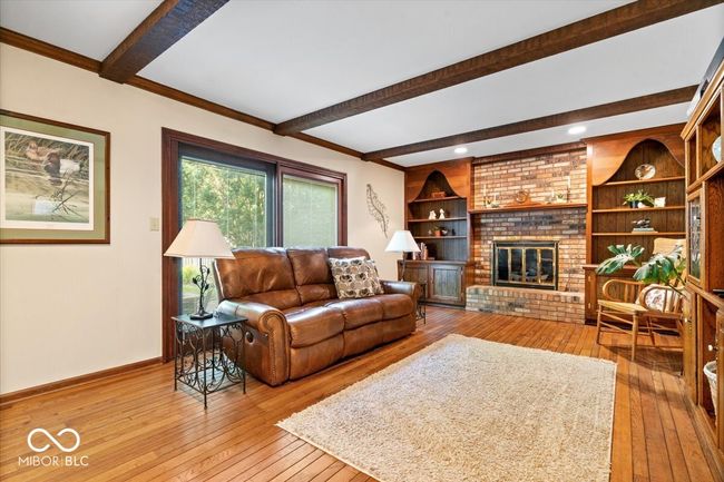 living area featuring wood-type flooring, beam ceiling, and a brick fireplace | Image 7