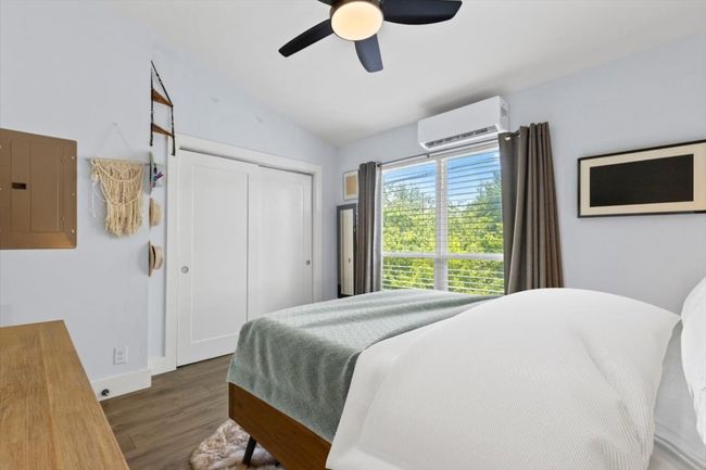 Bedroom with electric panel, an AC wall unit, wood finished floors, lofted ceiling, and a ceiling fan | Image 15