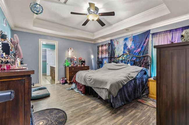 Bedroom with hardwood / wood-style floors, connected bathroom, ceiling fan, a tray ceiling, and crown molding | Image 14