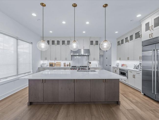 Kitchen featuring light countertops, a large island with sink, a sink, stainless steel built in fridge, and under cabinet range hood | Image 5