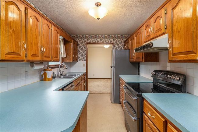 Kitchen with stainless steel appliances, under cabinet range hood, wallpapered walls, brown cabinets, and a textured ceiling | Image 11