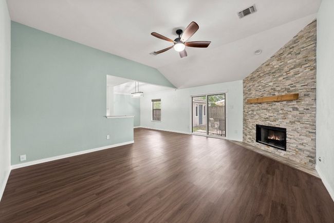 Unfurnished living room with a ceiling fan, vaulted ceiling, a fireplace, dark wood-type flooring, and baseboards | Image 5
