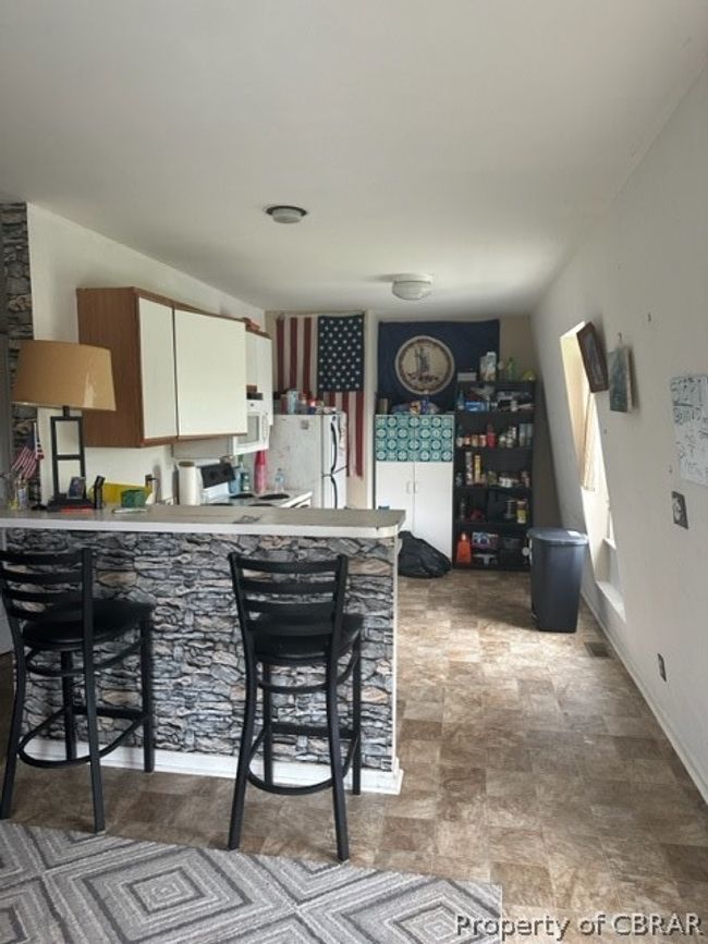 Kitchen with light tile patterned flooring, white cabinetry, kitchen peninsula, refrigerator, and a kitchen breakfast bar | Image 20
