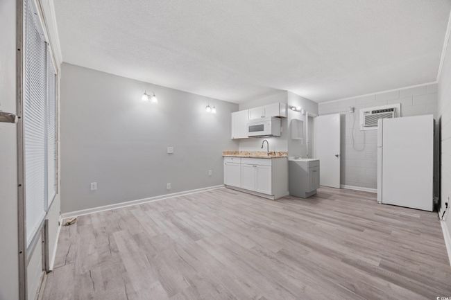 Kitchen featuring white appliances, light wood finished floors, light countertops, a sink, and a textured ceiling | Image 5