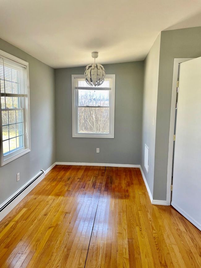 Unfurnished room featuring wood-type flooring, a baseboard radiator, plenty of natural light, and a chandelier | Image 8