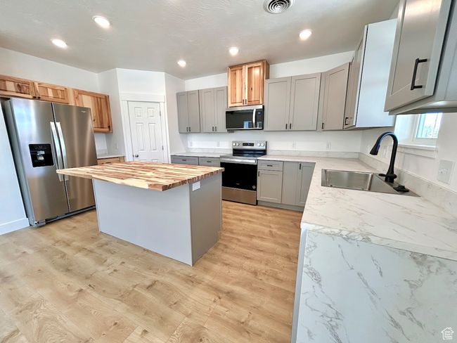 Kitchen featuring gray cabinets, butcher block counters, stainless steel appliances, a kitchen island, and a sink | Image 4