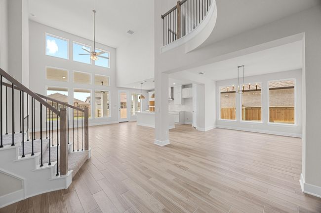 Unfurnished living room with a ceiling fan, light wood finished floors, baseboards, stairway, and a towering ceiling | Image 5