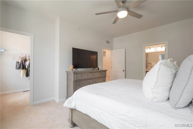 Bedroom with a spacious closet, visible vents, ensuite bath, baseboards, and light colored carpet | Image 31