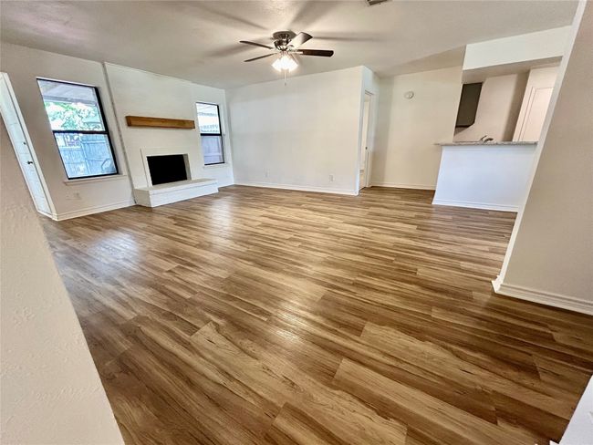 Unfurnished living room featuring a ceiling fan, wood finished floors, a fireplace with raised hearth, and baseboards | Image 4