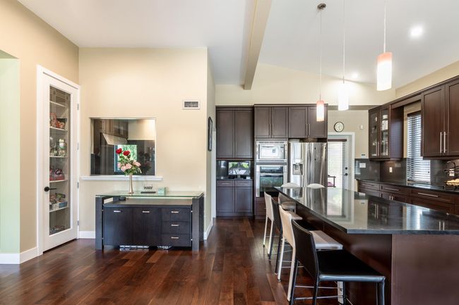 Kitchen featuring appliances with stainless steel finishes, dark wood-type flooring, dark brown cabinets, glass insert cabinets, and a kitchen bar | Image 16