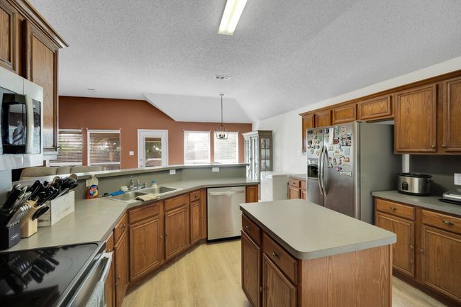 Kitchen featuring stainless steel appliances, light wood-style floors, vaulted ceiling, brown cabinets, and a textured ceiling | Image 15