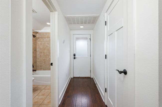 This entryway leads to the private guest accommodations, featuring a sleek, clean design with wood flooring and white accents. A frosted door adds privacy, while access to a full bathroom and additional rooms makes it a comfortable and self-contained space for visitors. | Image 28