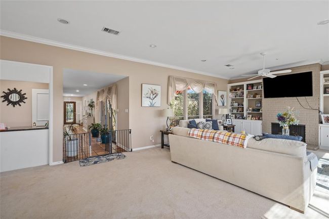 This spacious living area offers a cozy yet open feel, featuring a brick fireplace framed by built-in shelving for storage and display. Large windows allow for abundant natural light, while the neutral color palette and plush carpeting create a welcoming atmosphere. The room seamlessly connects to the foyer and kitchen, enhancing the home's flow. | Image 15