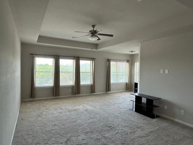 Unfurnished living room featuring a ceiling fan, carpet flooring, a tray ceiling, and baseboards | Image 24
