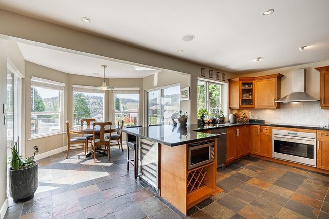 Kitchen with wall chimney exhaust hood, appliances with stainless steel finishes, brown cabinets, stone tile flooring, and recessed lighting | Image 9