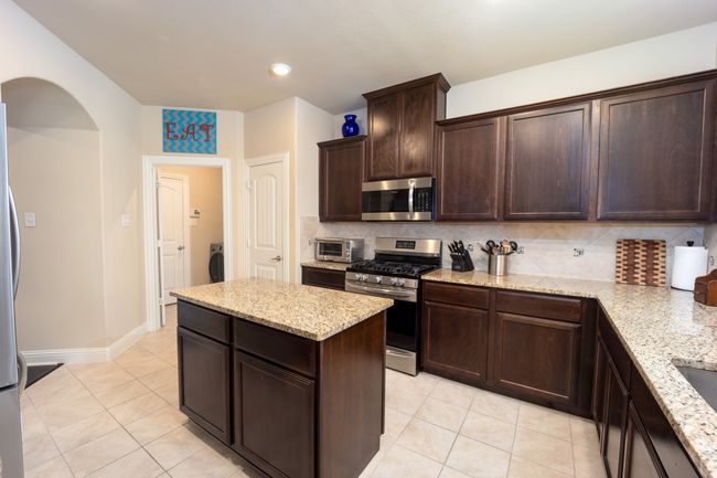 Kitchen with appliances with stainless steel finishes, light tile patterned floors, backsplash, dark brown cabinets, and recessed lighting | Image 7