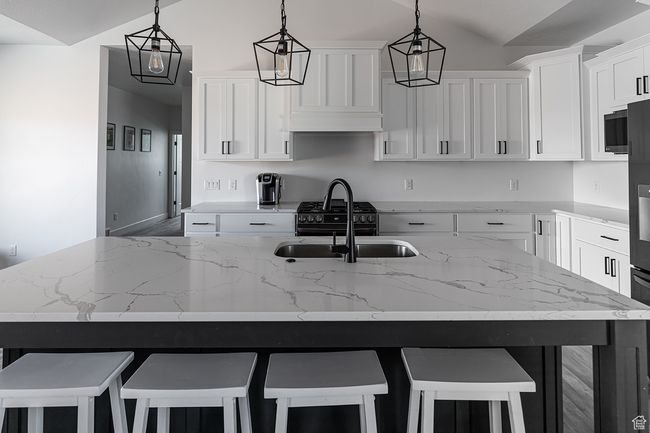 Kitchen featuring light stone countertops, a sink, decorative light fixtures, white cabinetry, and lofted ceiling | Image 6