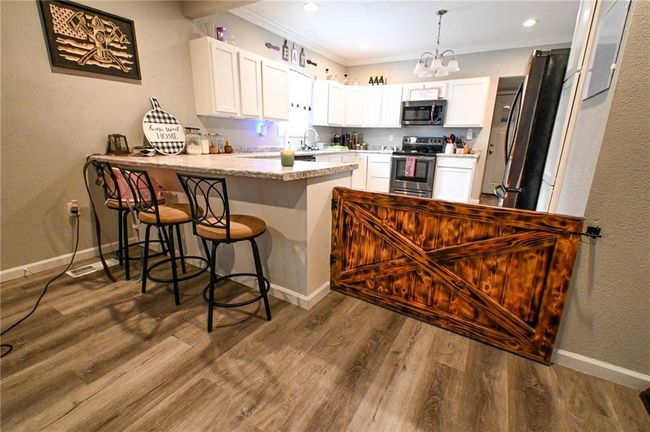 Kitchen featuring appliances with stainless steel finishes, a peninsula, white cabinetry, ornamental molding, and a chandelier | Image 15