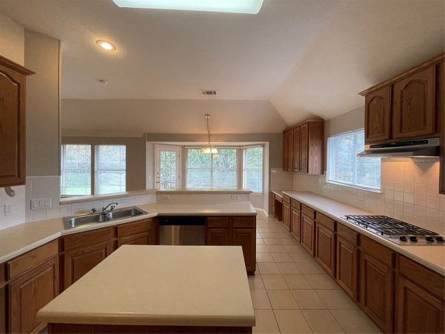Kitchen with dishwasher, cooktop, range hood, brown cabinetry, and vaulted ceiling | Image 11